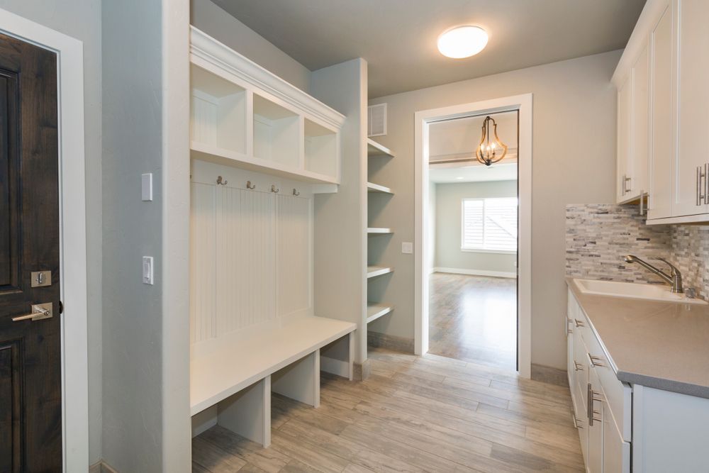 A bright mudroom with a built-in bench, cubbies, open shelving, and a laundry sink with white cabinets and tile backsplash.
