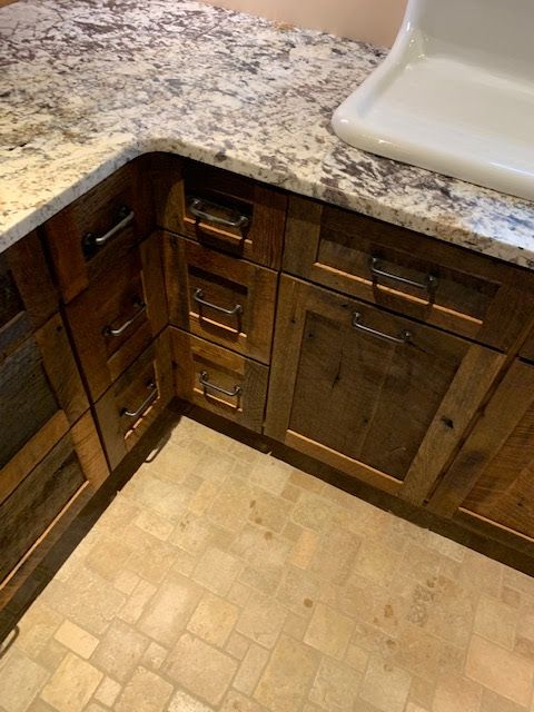 A high-angle view of rustic wooden kitchen cabinets with metal pulls, granite countertops, and a white sink.