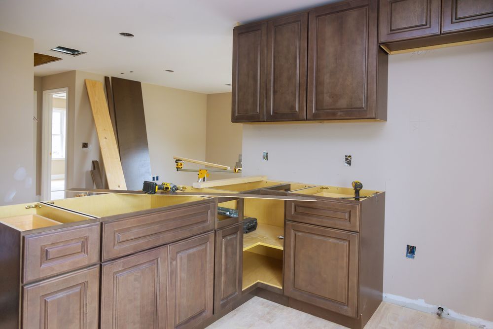 Kitchen under construction featuring installed dark wood cabinets and a base frame on a light, unfinished floor.