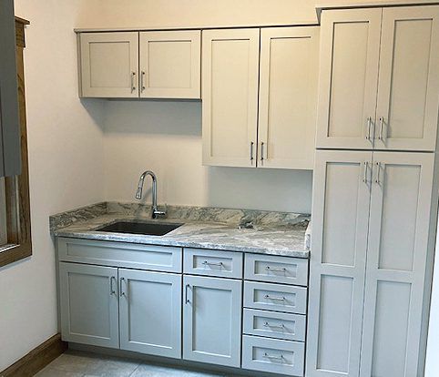 A small kitchen area with light gray cabinets, a granite countertop, a stainless steel sink, and a tall pantry cabinet.
