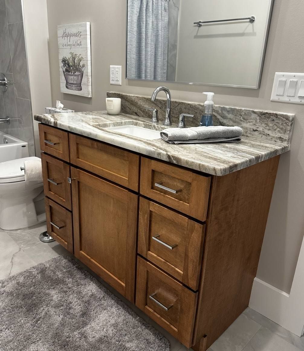A bathroom vanity with a granite countertop, sink, and faucet, featuring wooden cabinets with metal hardware.