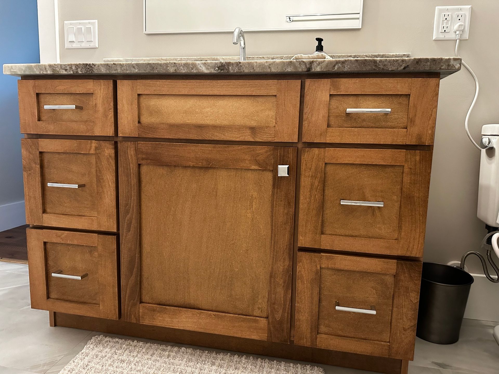 A wooden bathroom vanity with six drawers and a center cabinet door, topped with a stone counter and sink.
