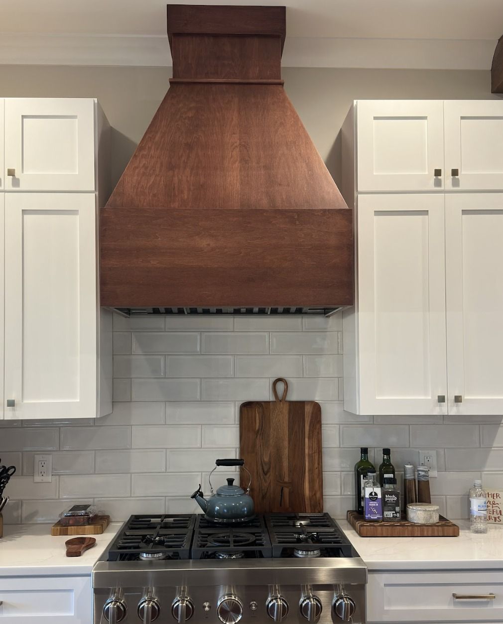 A range stove topped with a large, wooden vent hood between white cabinets over a subway tile backsplash.