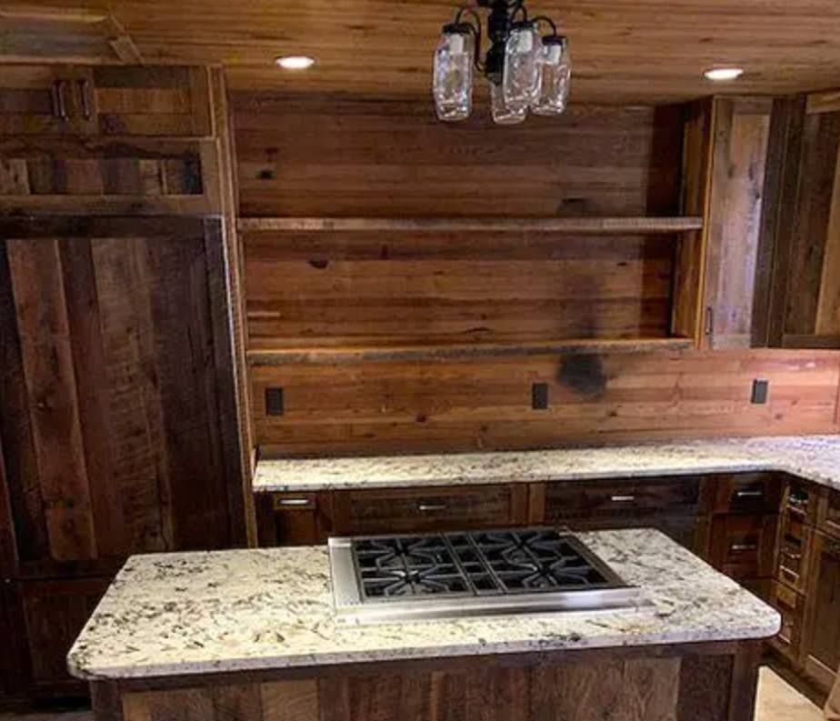A rustic kitchen featuring wooden walls and cabinetry, speckled granite countertops, a central island, and mason jar light.