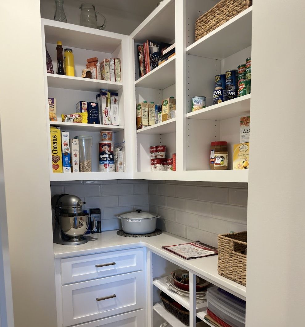 A well-organized pantry with white cabinets, shelves stocked with various food containers, and a countertop with appliances.