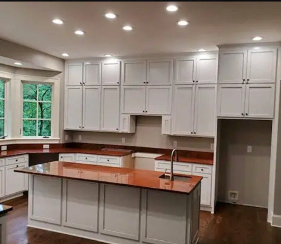 A kitchen with white cabinets, dark wood countertops, an island with a sink, and recessed lighting.