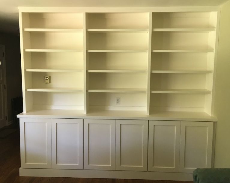 A built-in wall unit featuring white base cabinets with six cabinet doors below three sections of open shelving.