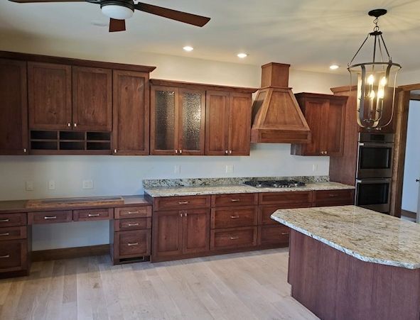 A modern kitchen with brown wood cabinets, granite countertops, a built-in oven, and a hanging lantern light fixture.