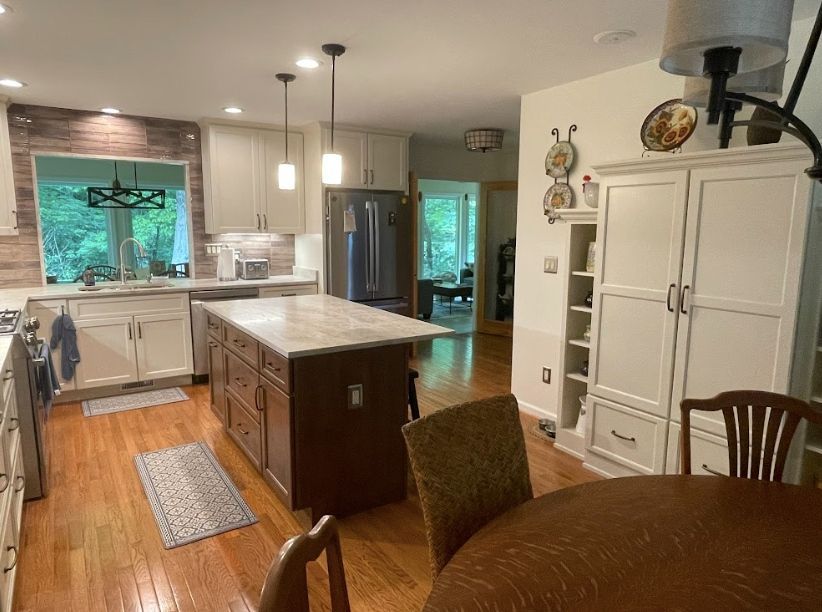 A modern kitchen with a center island, white cabinetry, hardwood floors, and a dining area with a round table.
