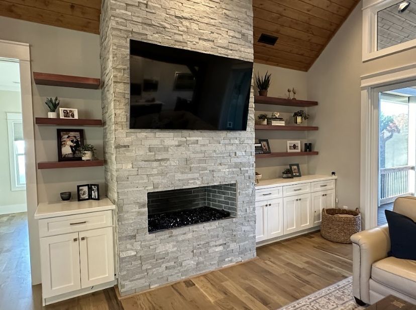 A living room featuring a stone fireplace with a mounted television, flanked by white cabinetry and wood shelves.
