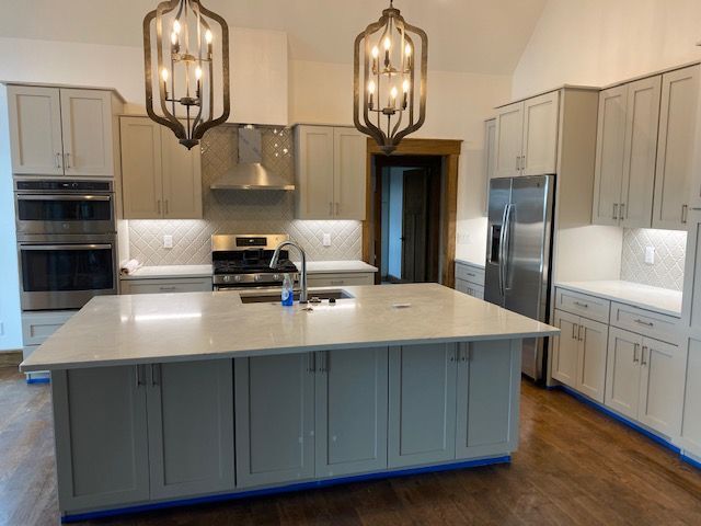 A modern kitchen with light gray cabinetry, stainless steel appliances, a large central island, and two pendant lights.