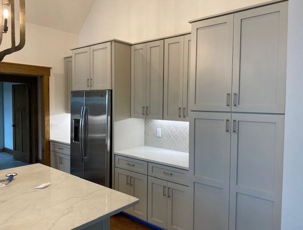 A modern kitchen featuring grey shaker-style cabinets, a stainless steel refrigerator, and white marble countertops.