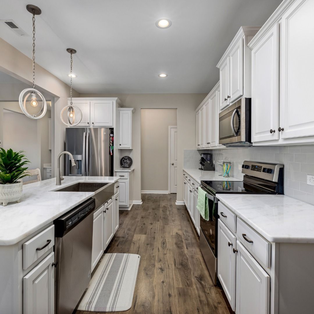 A bright, modern kitchen featuring white cabinets, stainless steel appliances, a marble-topped island, and wood flooring.