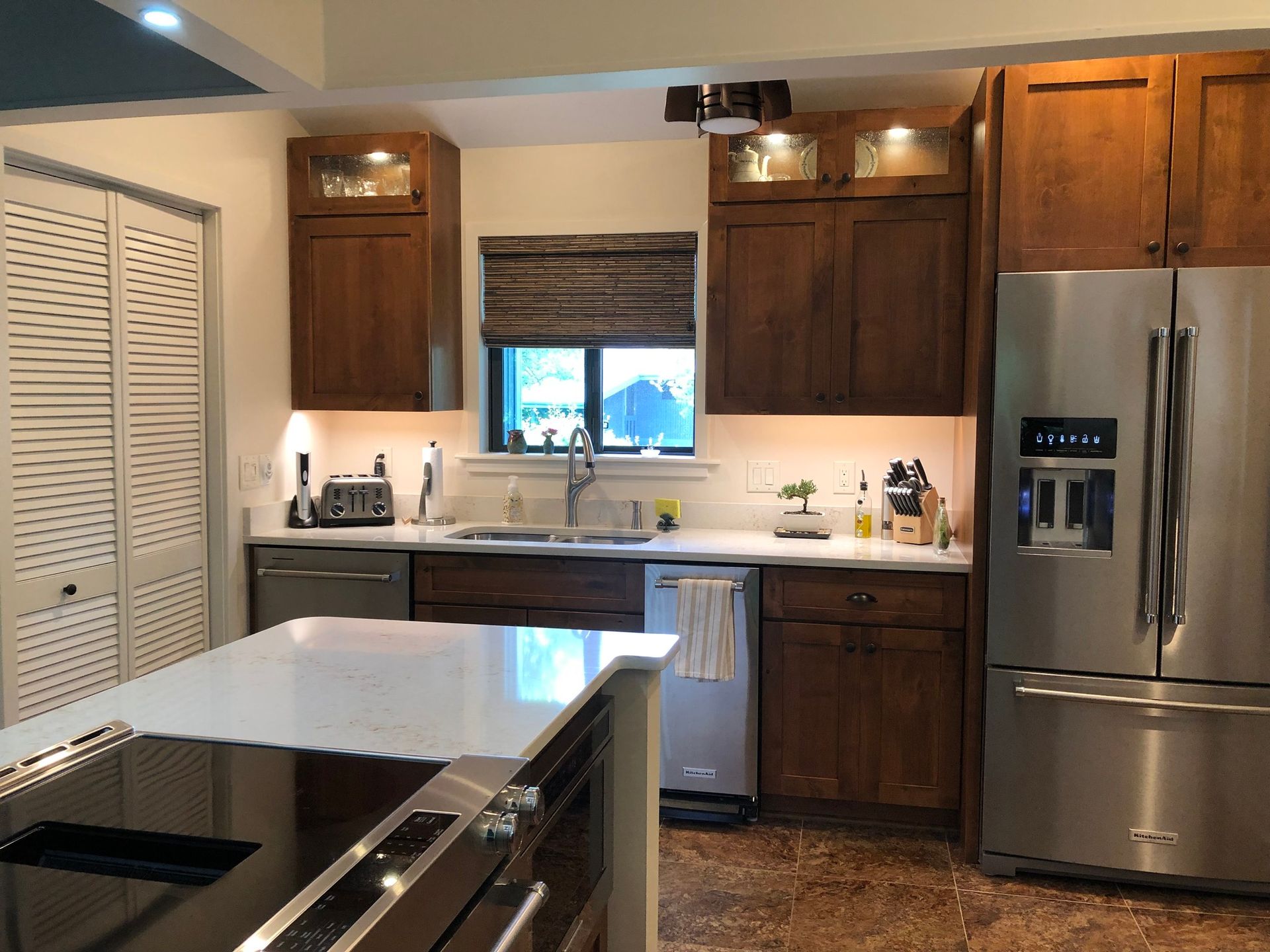 A kitchen with dark wood cabinets, stainless steel appliances, white countertops, and a central kitchen island.