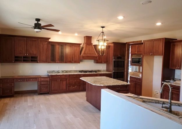 A large kitchen featuring dark cherry wood cabinets, a center island with granite countertops, and light hardwood floors.