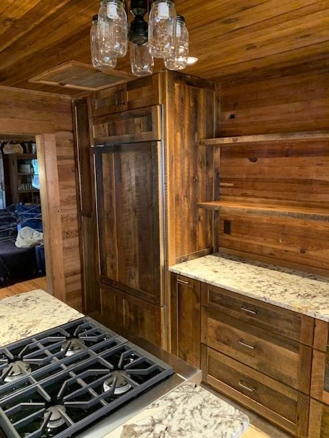 A rustic kitchen with wood-paneled walls, granite countertops, a gas cooktop, and a mason jar light fixture.