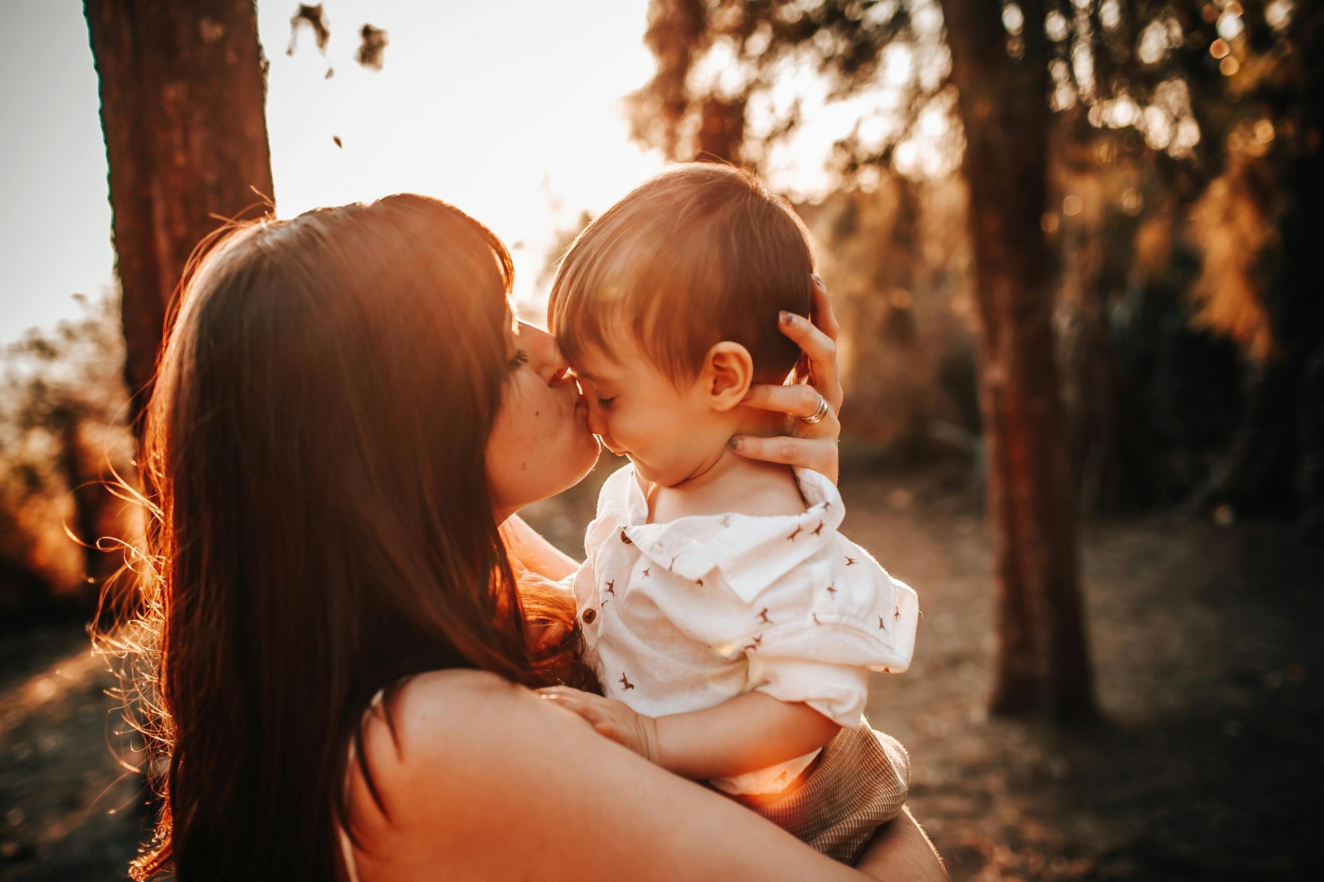 A mother is kissing her baby while the sun shines on them