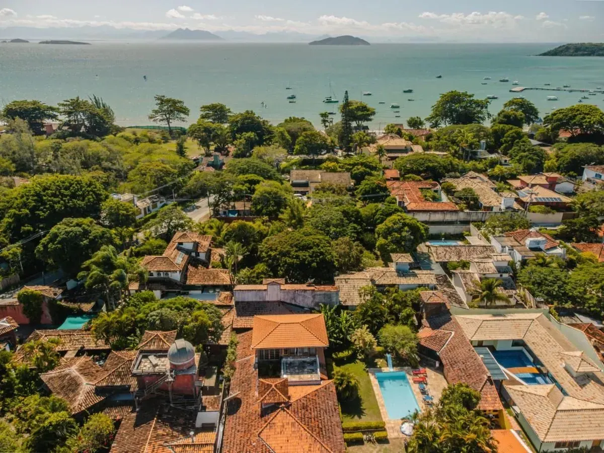 Barrio costero con tejados de tejas, árboles frondosos y una piscina azul junto al mar.