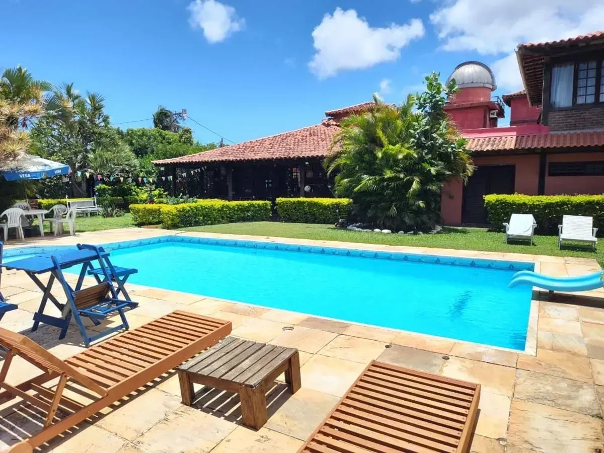 Resort pool with blue water, lounge chairs, and a red-tiled building under a sunny sky