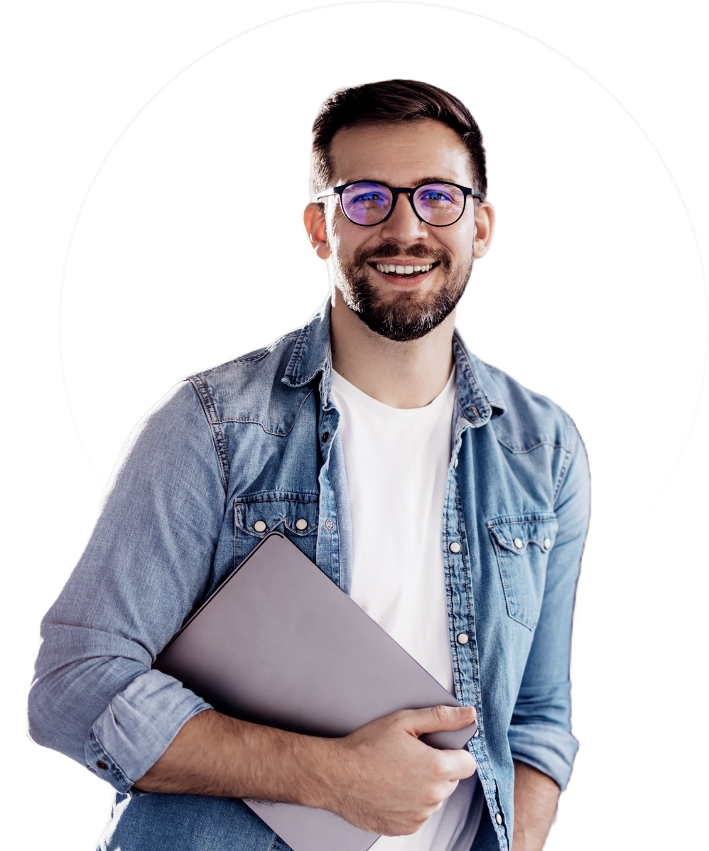 Persona sonriente sosteniendo una computadora portátil, con gafas, camisa vaquera sobre una camiseta blanca sobre un fondo blanco.