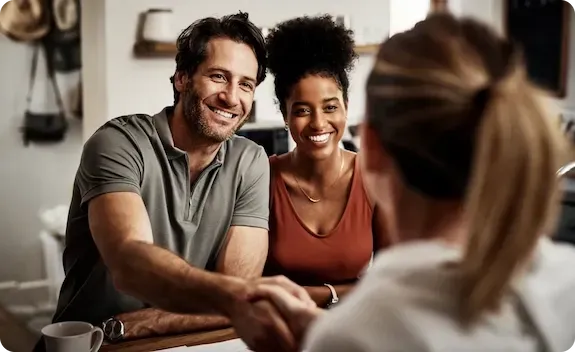Três pessoas sorrindo em uma reunião informal, sentadas em frente a uma mulher em primeiro plano.