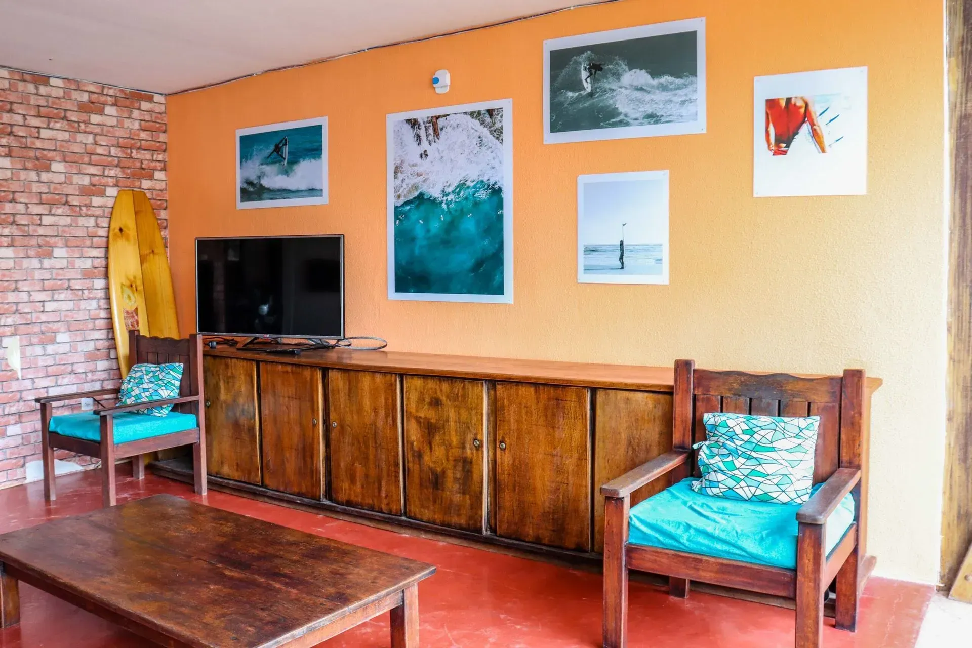 Acogedora sala de estar con pared naranja, armario de madera, televisor, cuadro con motivos marinos y dos sillas azules.