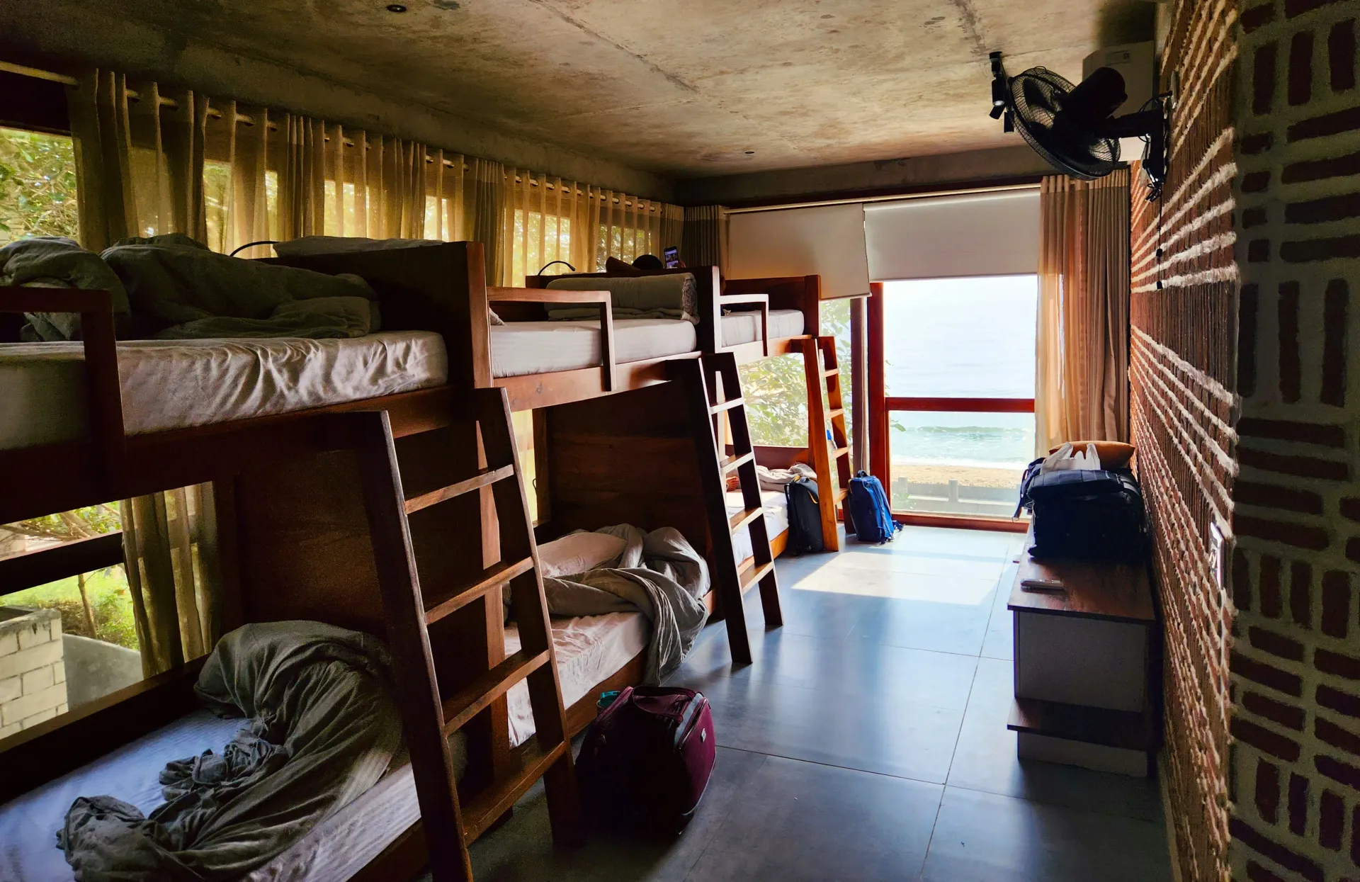 Habitación de residencia estudiantil con literas de madera, escritorios y una ventana luminosa en el extremo opuesto.