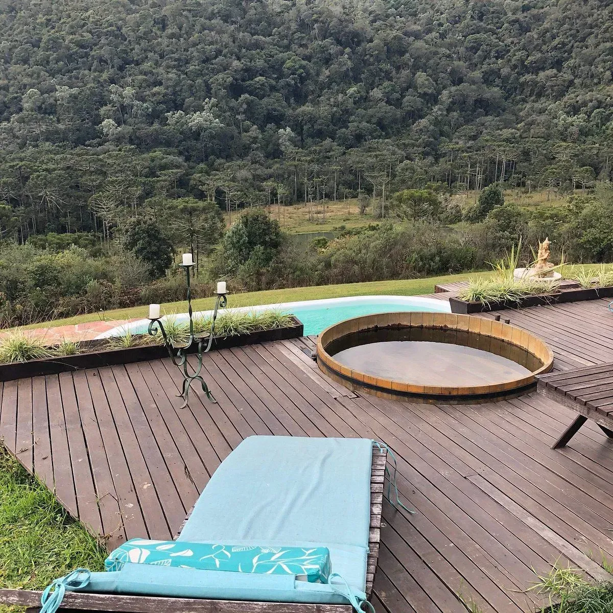 Terraza de madera con tumbona turquesa y jacuzzi redondo con vistas a un valle boscoso exuberante.