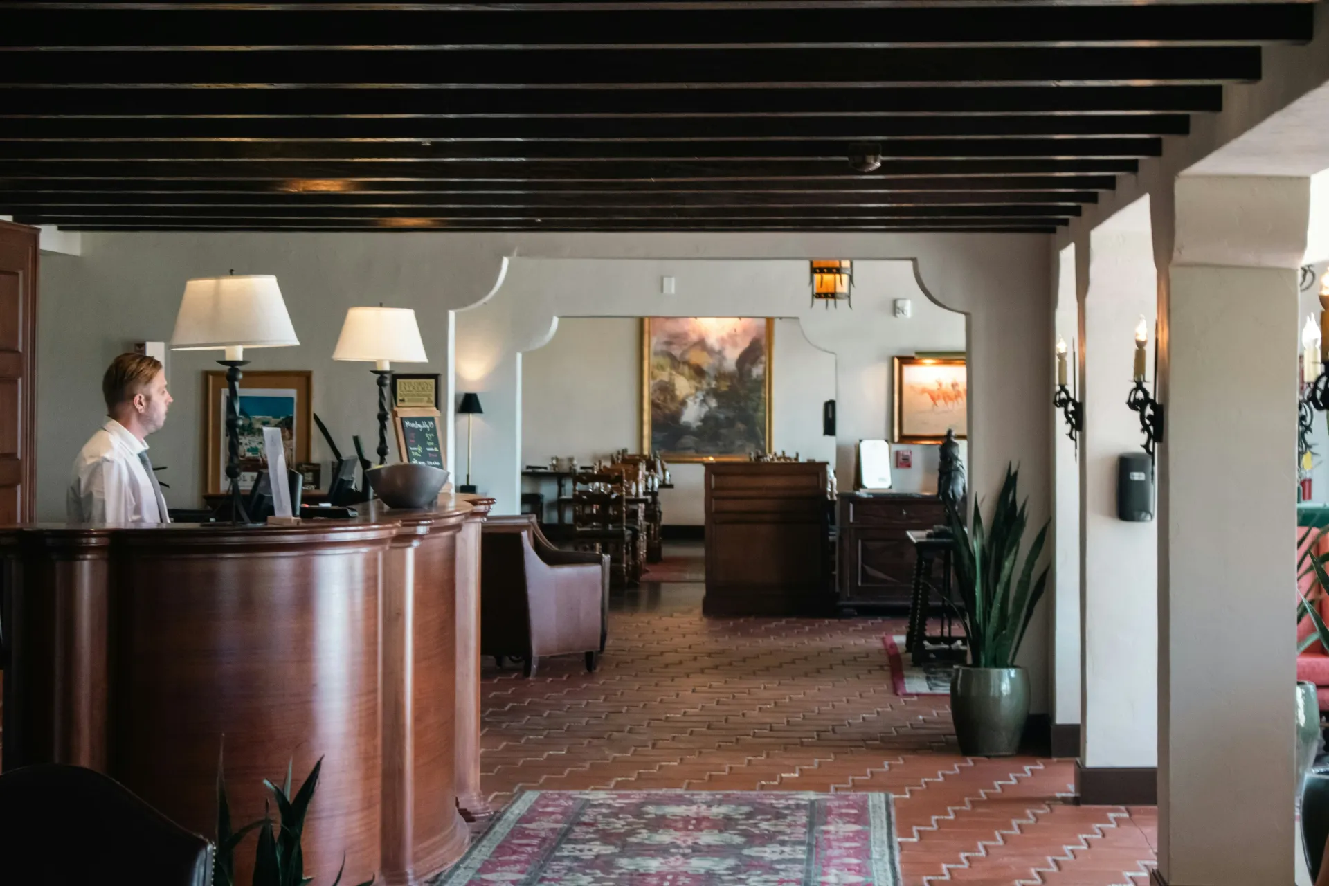 Vestíbulo del hotel con vigas de madera, mostrador de recepción, lámparas, alfombra y zona de estar.