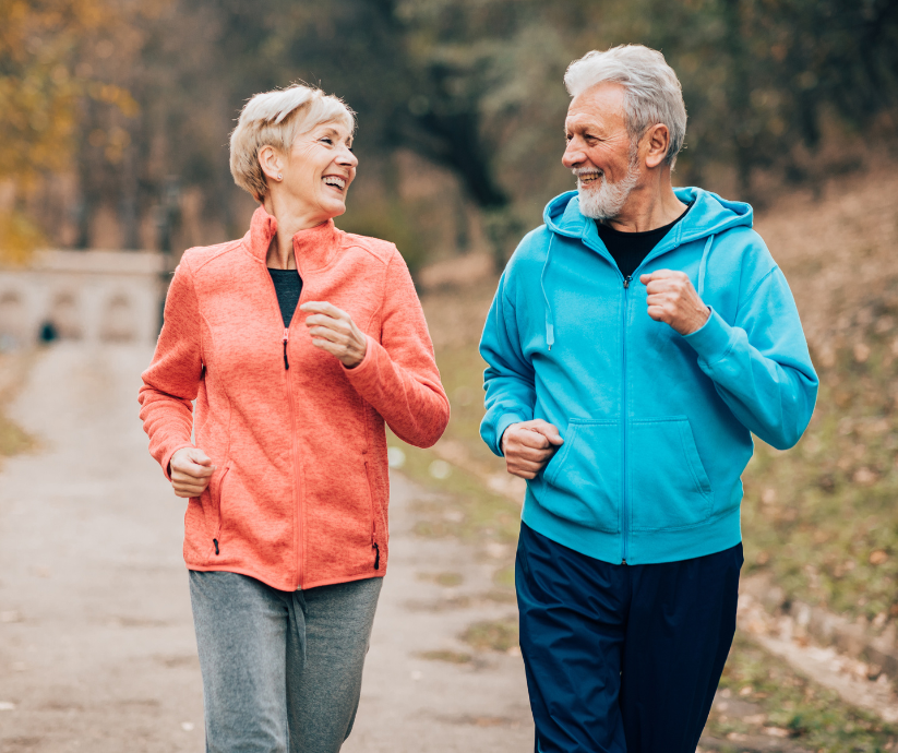 Older couple jogging together and smiling outdoors.