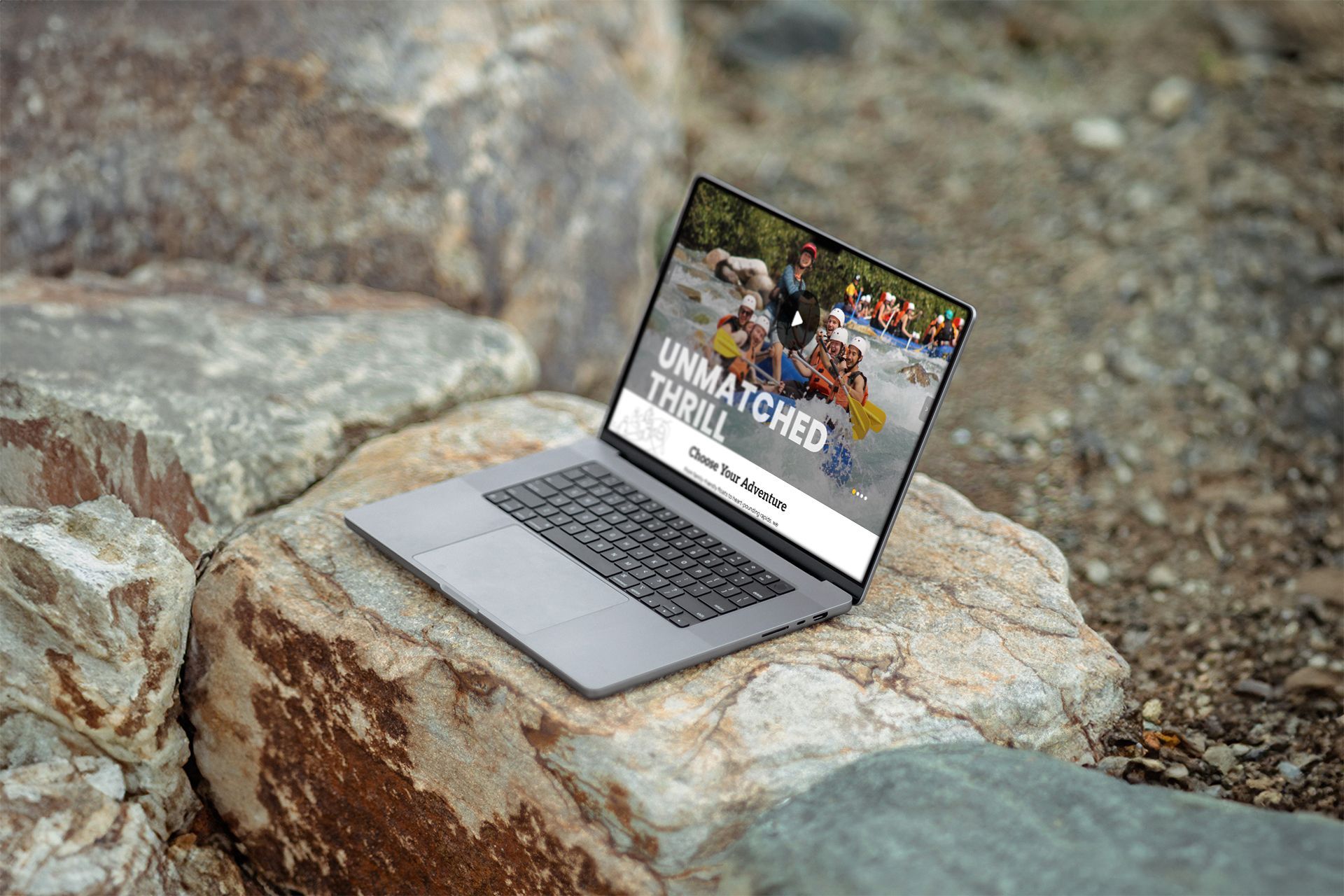 Laptop displaying rafting adventure website, resting on rocks.