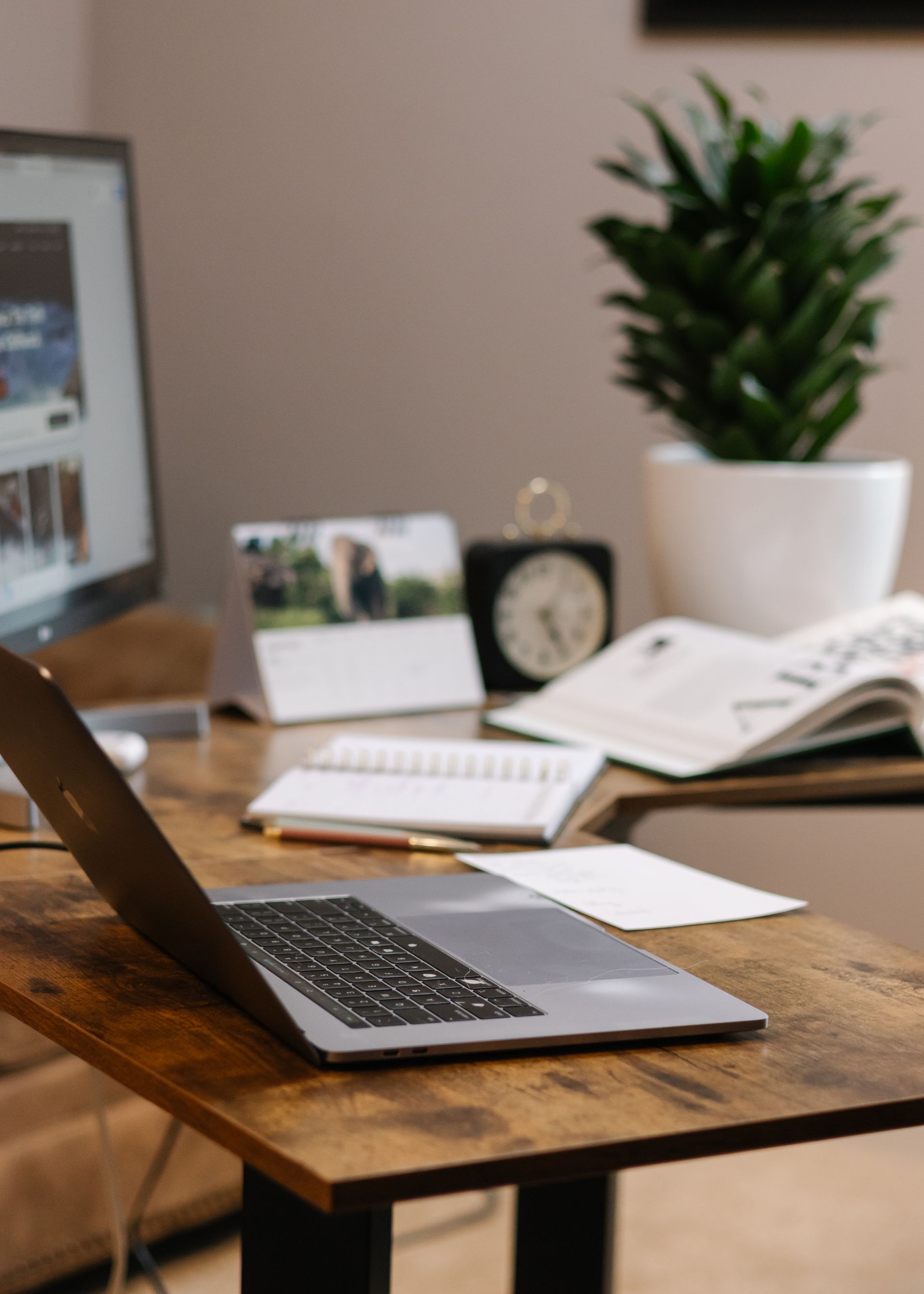 Laptop, monitor, and desk accessories on a wooden desk with a plant.