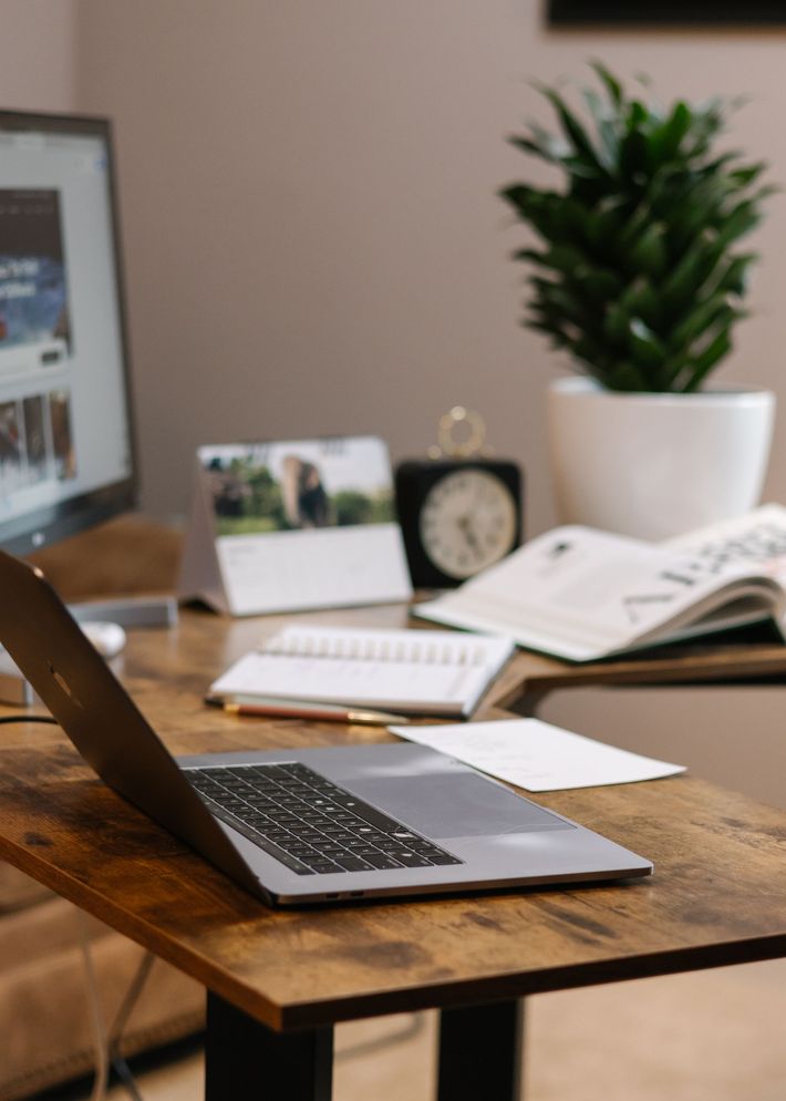 Laptop, monitor, and desk accessories on a wooden desk with a plant.