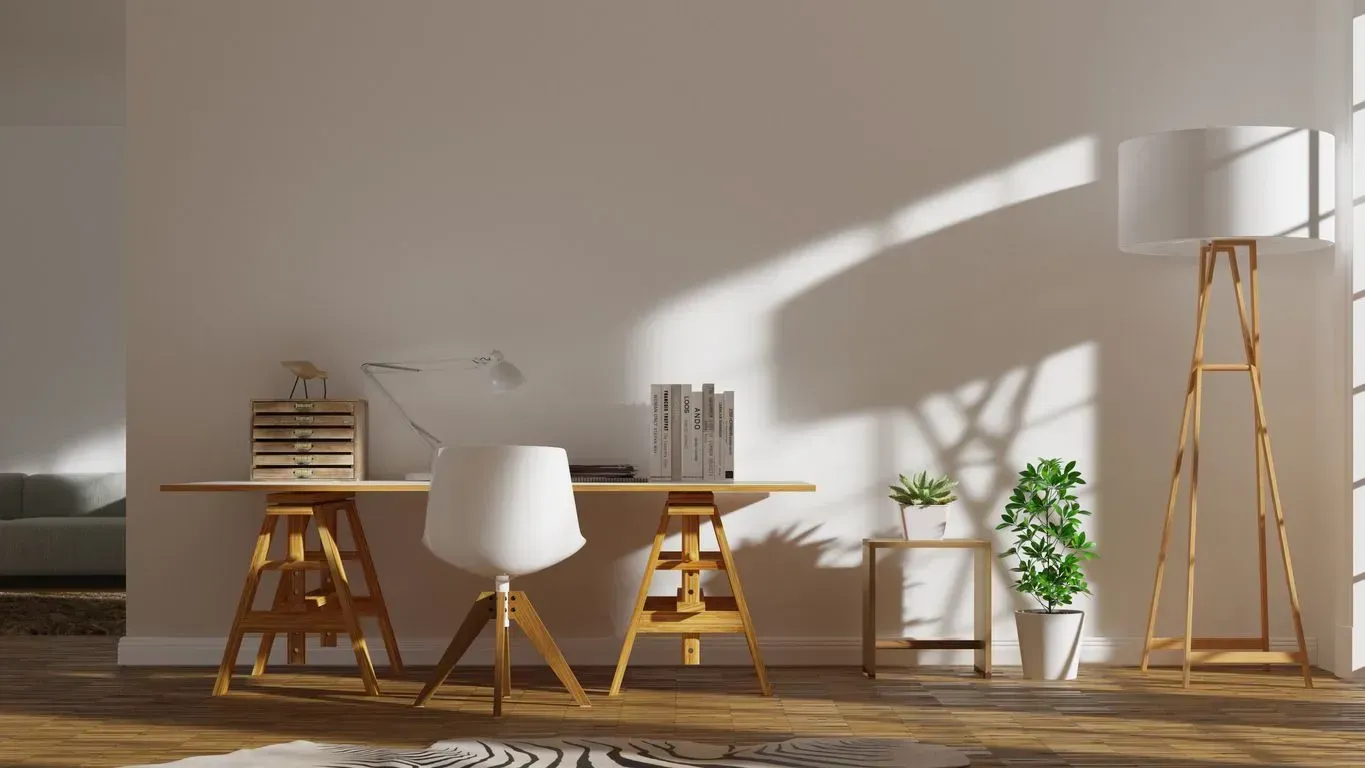 Modern sunlit room with wooden desks, white chairs, plants, and a tall floor lamp on a patterned rug.