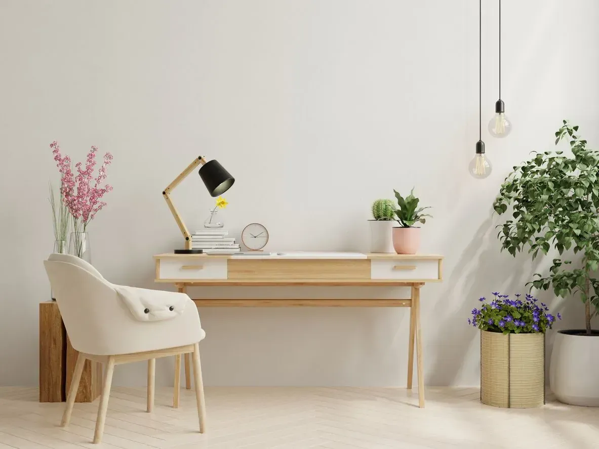 Minimalist home office with a wooden desk, cream chair, plants, and hanging lights
