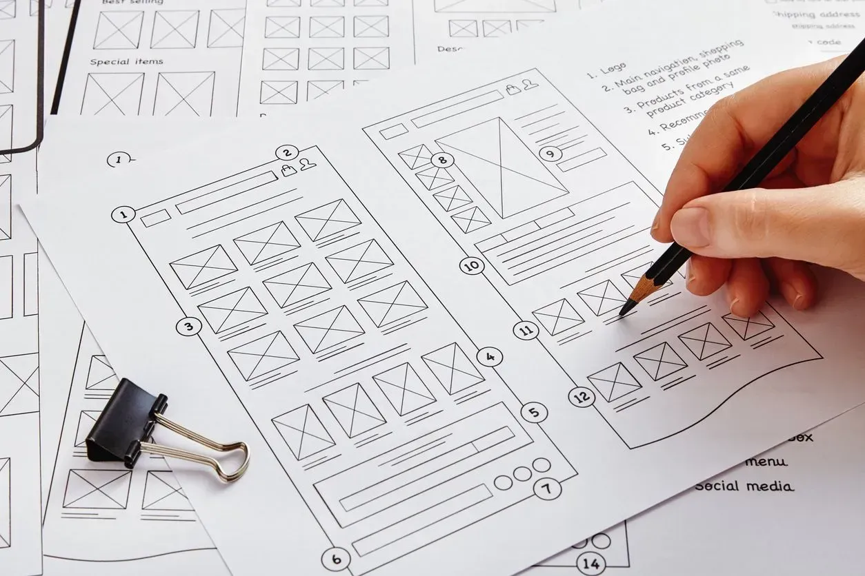 Hand sketching website wireframes on a table with black-and-white design mockups and binder clip