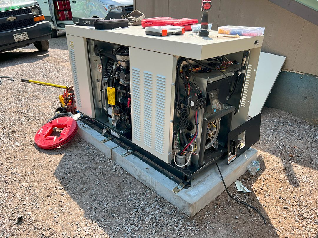 Generator with open panels, showing internal components, sits on a concrete pad outdoors. Tools and parts are visible on top.