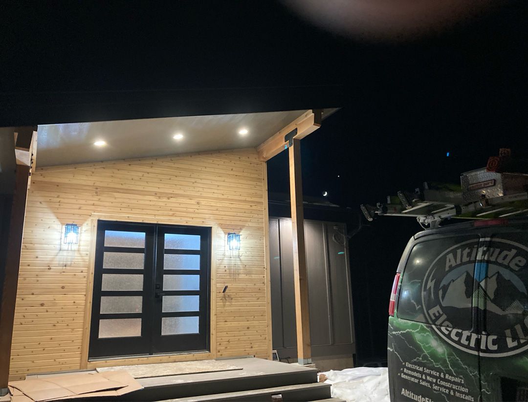 Exterior of a building with illuminated entry lights and a black door. A van with 