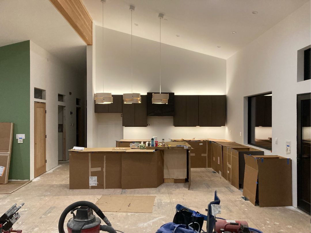 Kitchen under construction with cardboard-covered cabinets. Brown, white, green walls, wooden beam, and lights.
