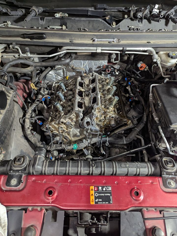 Engine bay with the engine removed, exposing hoses, wiring, and metal components in a red car.