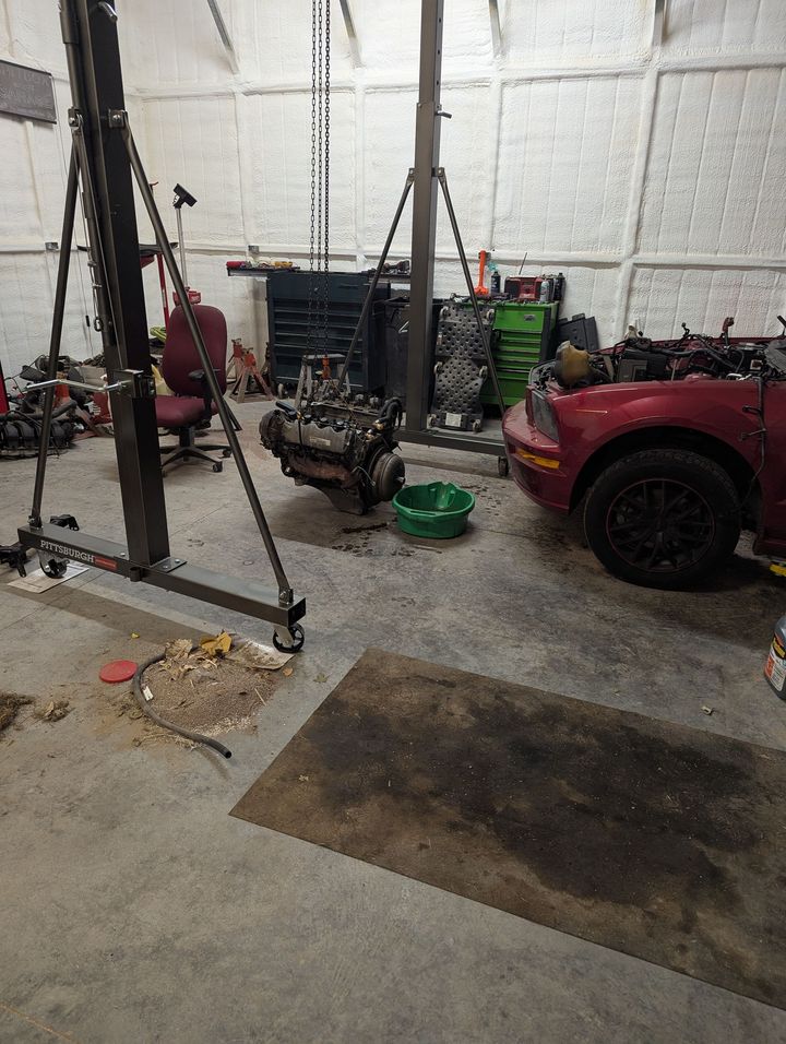 Garage workshop with a red vehicle, engine parts, and tools around a car lift.