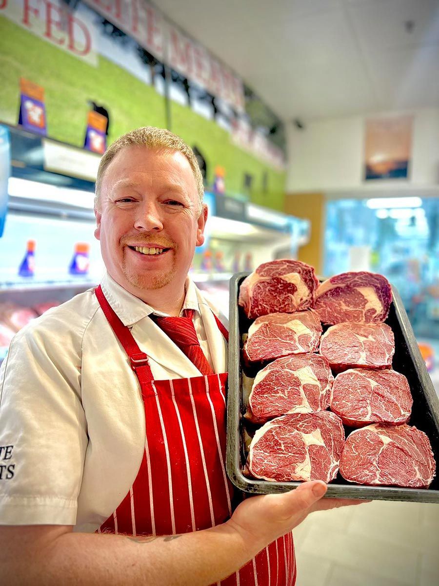 Man In A Red Apron Is Holding A Tray Of Meat — Elite Meats in Holt, ACT