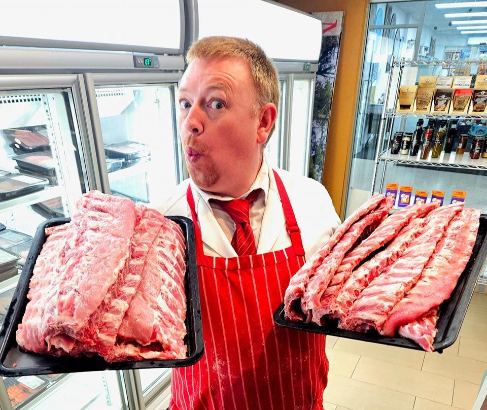 Man In A Red Apron Is Holding Two Trays Of Meat At The Shop — Elite Meats in Holt, ACT