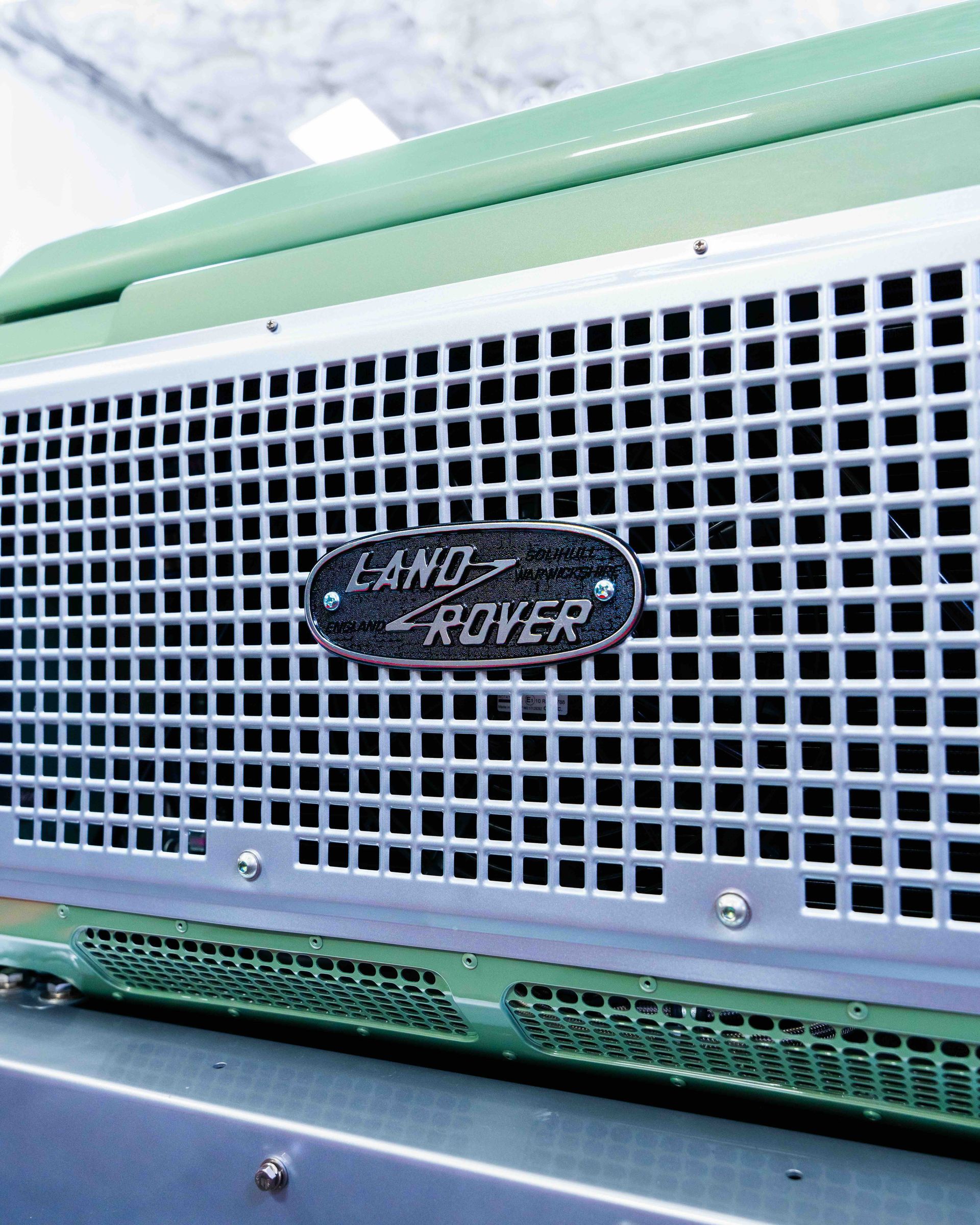 Close-up of a green Land Rover grille with the badge centered on a white mesh front panel.