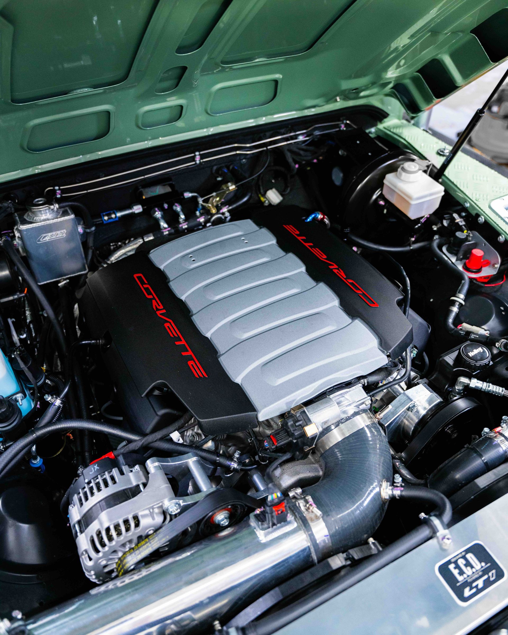 Car engine bay with black and silver intake cover under a green hood