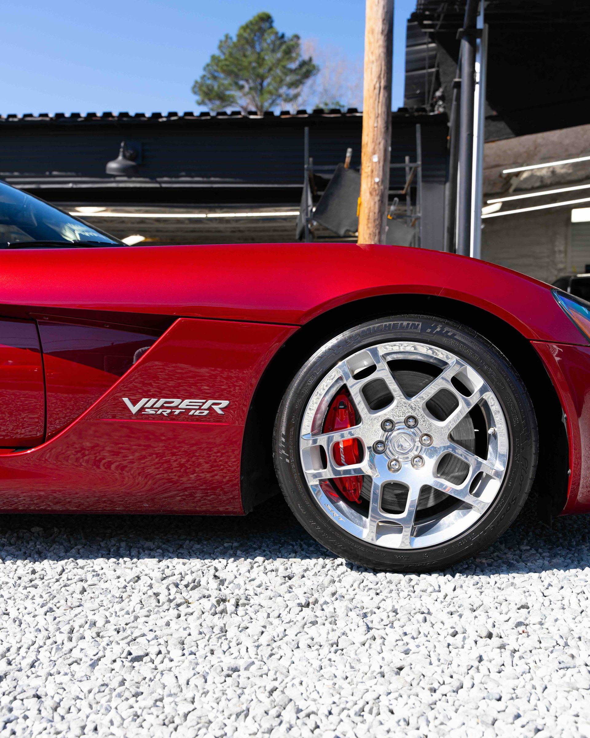 Red sports car side view with chrome wheel parked outdoors in sunlight