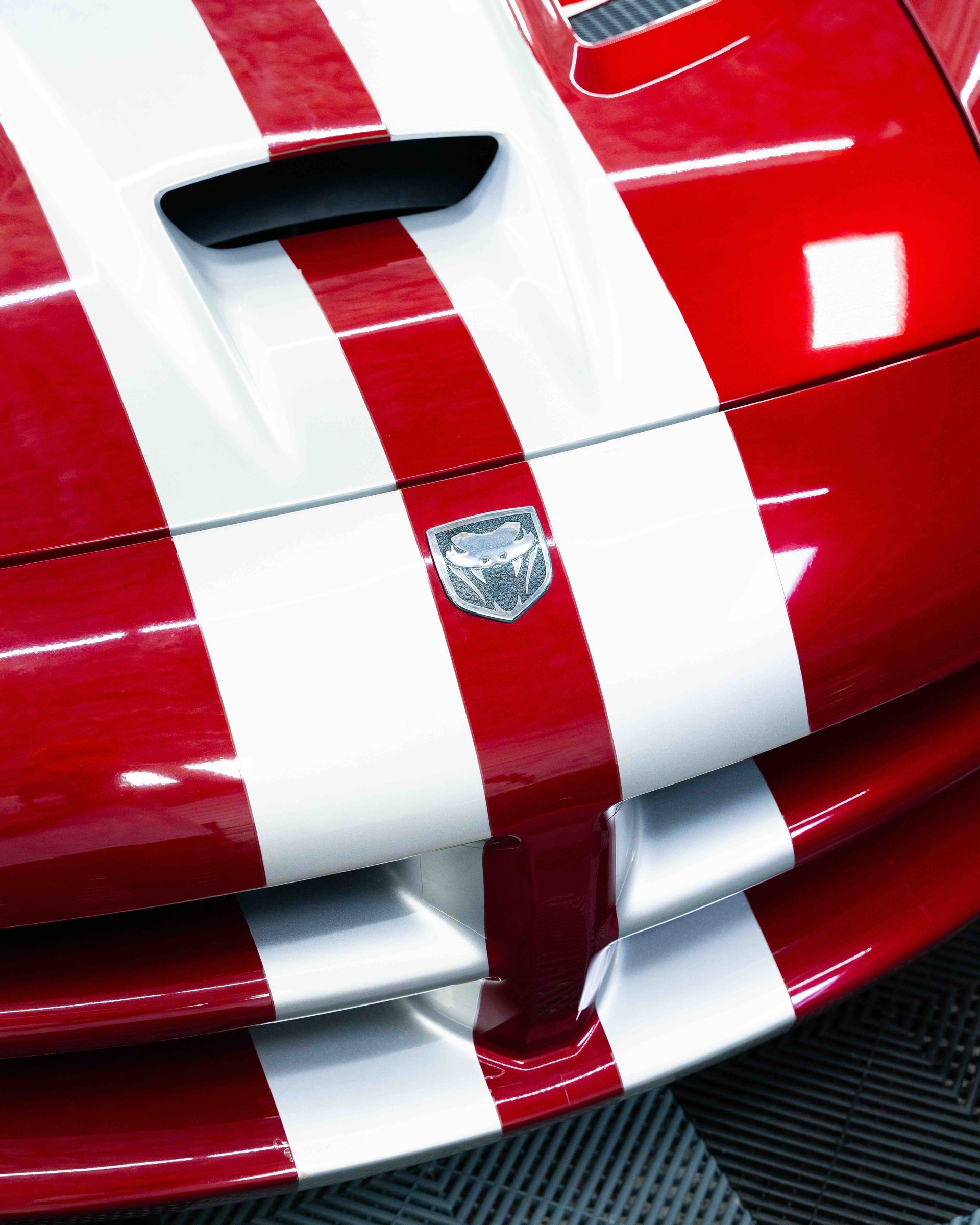 Close-up of a red sports car hood with white racing stripes and a badge.