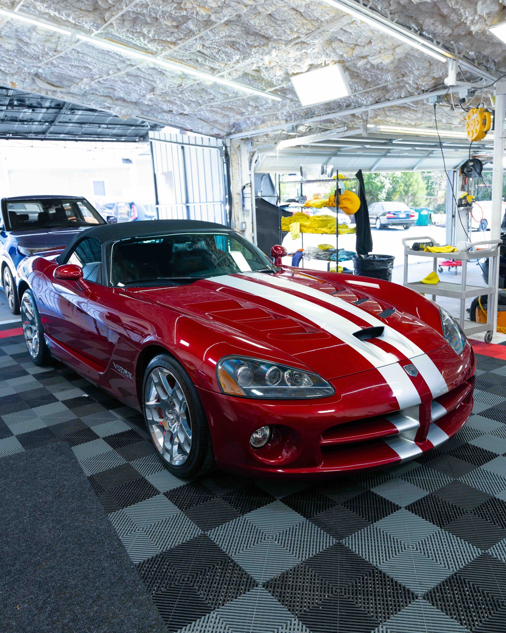 Red sports car with white racing stripes displayed in a showroom beside a black car.