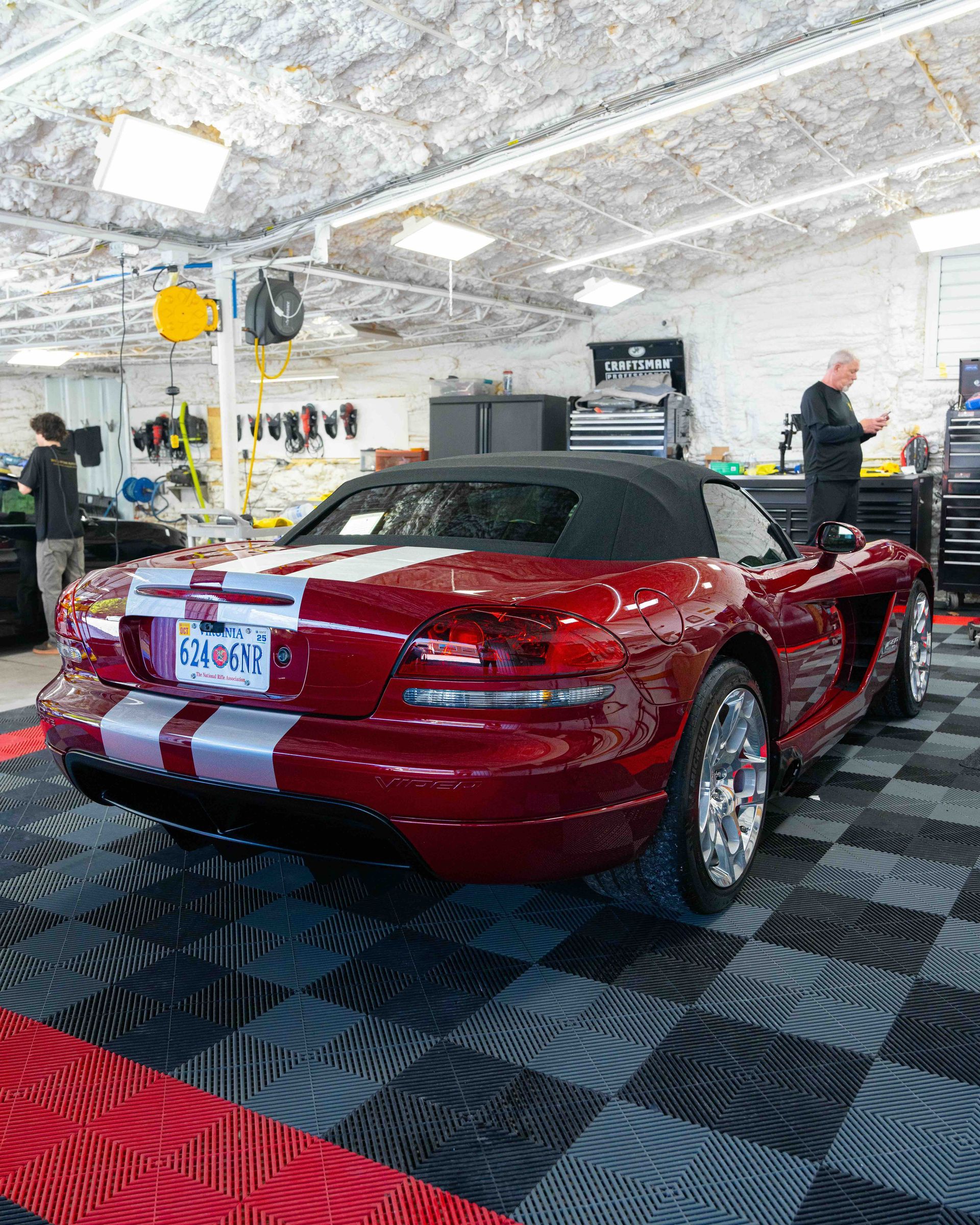 Red convertible sports car in a garage, with white racing stripes and a black soft top.