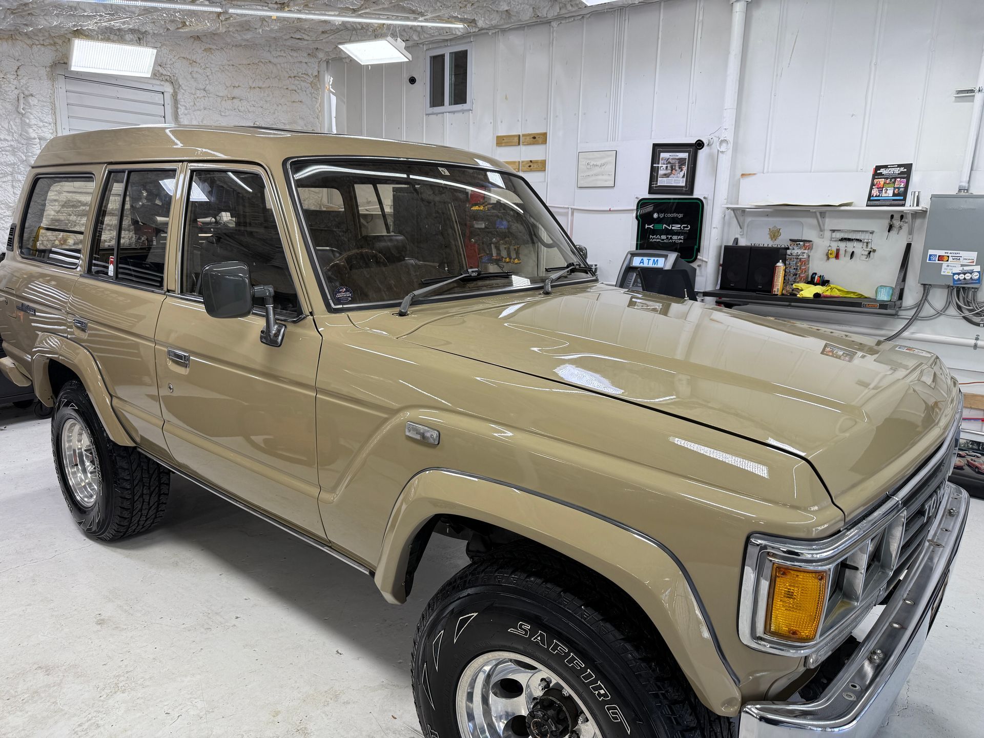 A tan vintage Toyota Land Cruiser parked inside a brightly lit garage or workshop.